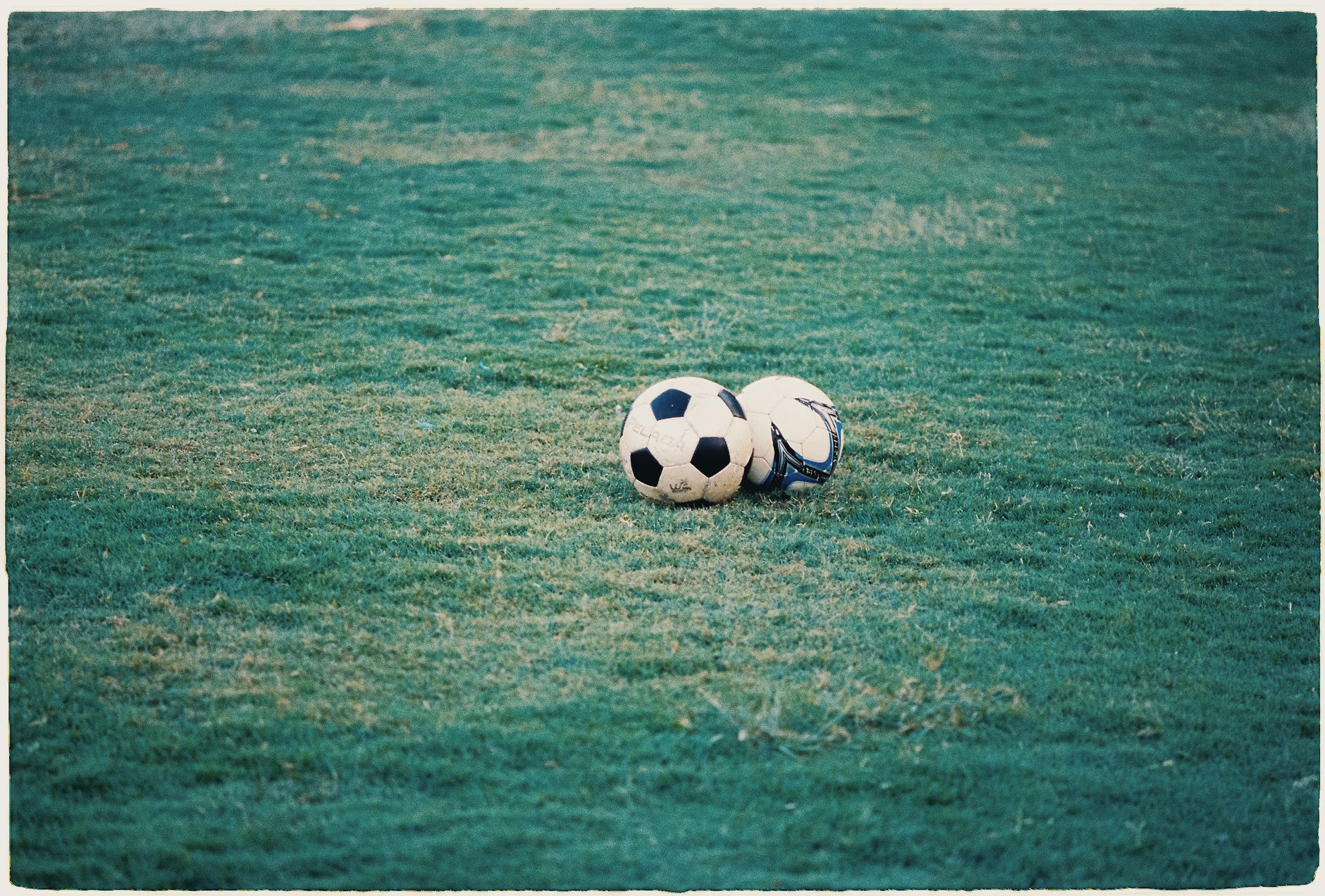 Imagem ilustrativa: Duas bolas de futebol repousando em um campo gramado.