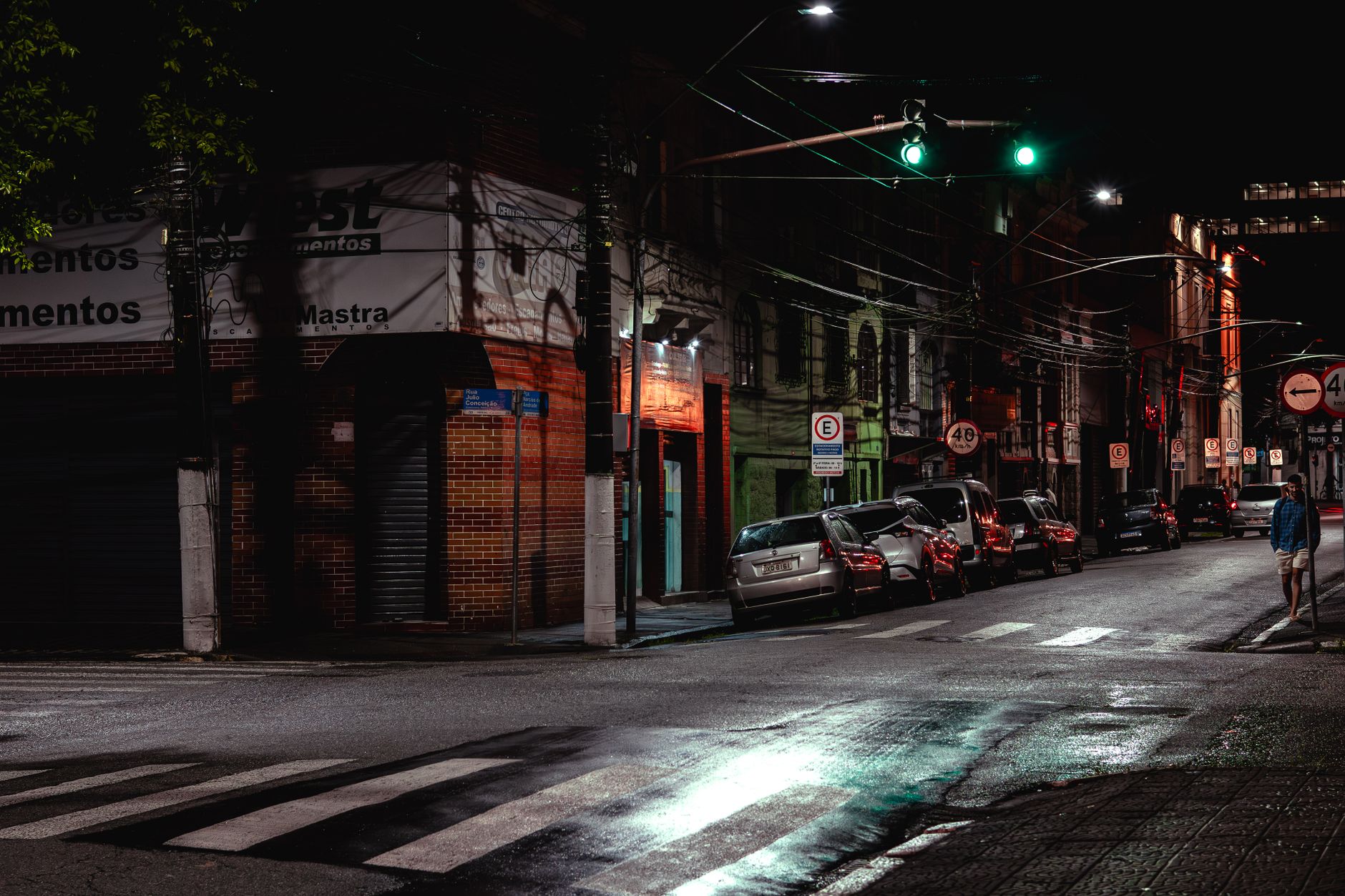 Imagem ilustrativa: Rua urbana durante a noite com veículos estacionados sob iluminação pública e asfalto úmido.