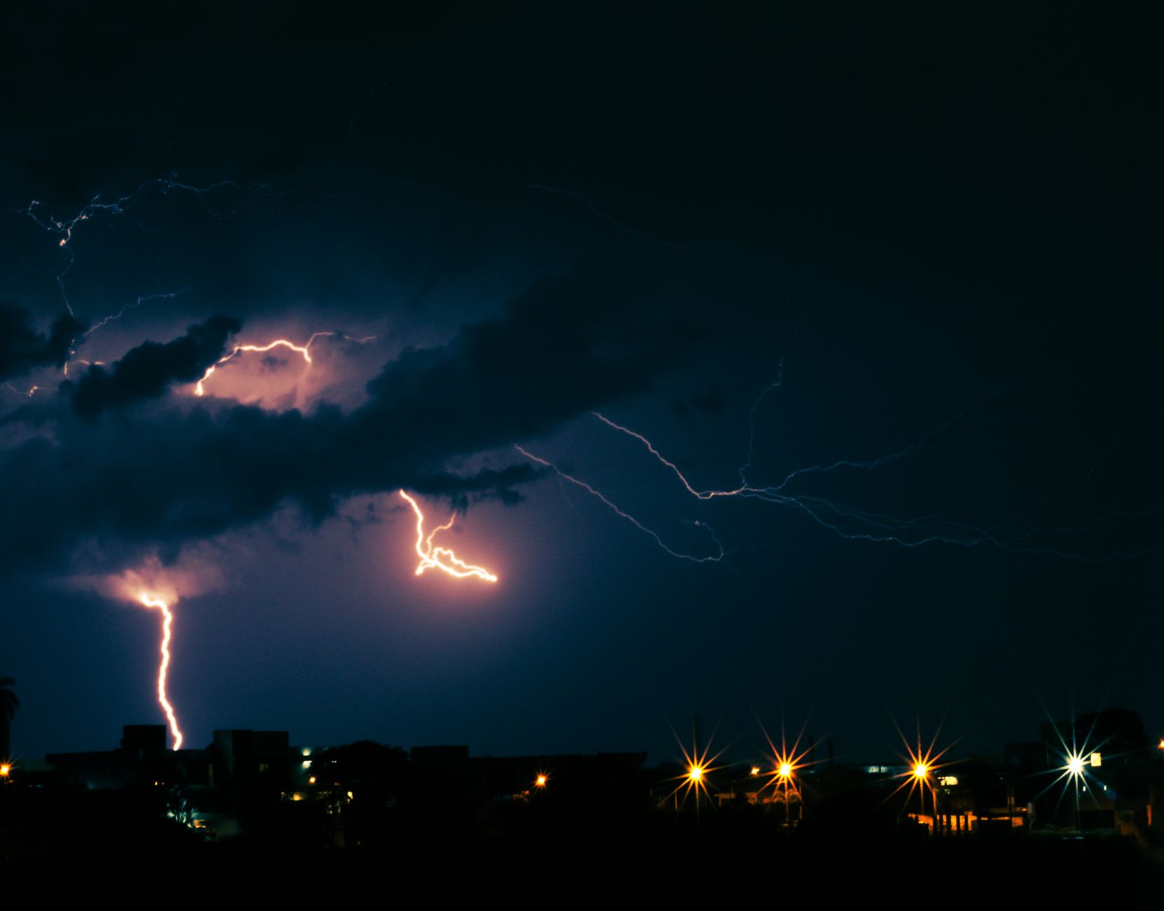 Imagem ilustrativa: Relâmpagos iluminam o céu escuro sobre a cidade à noite, capturando a energia de uma tempestade urbana.