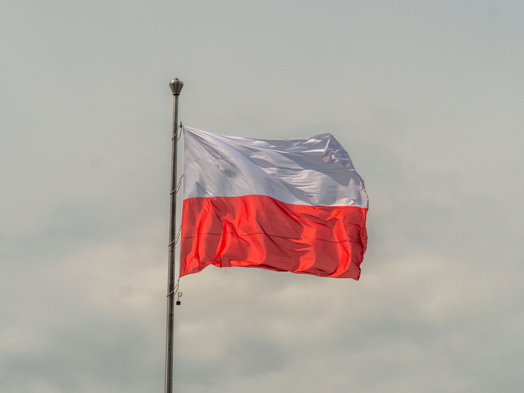 Imagem ilustrativa: A bandeira nacional polonesa tremulando contra um céu nublado.