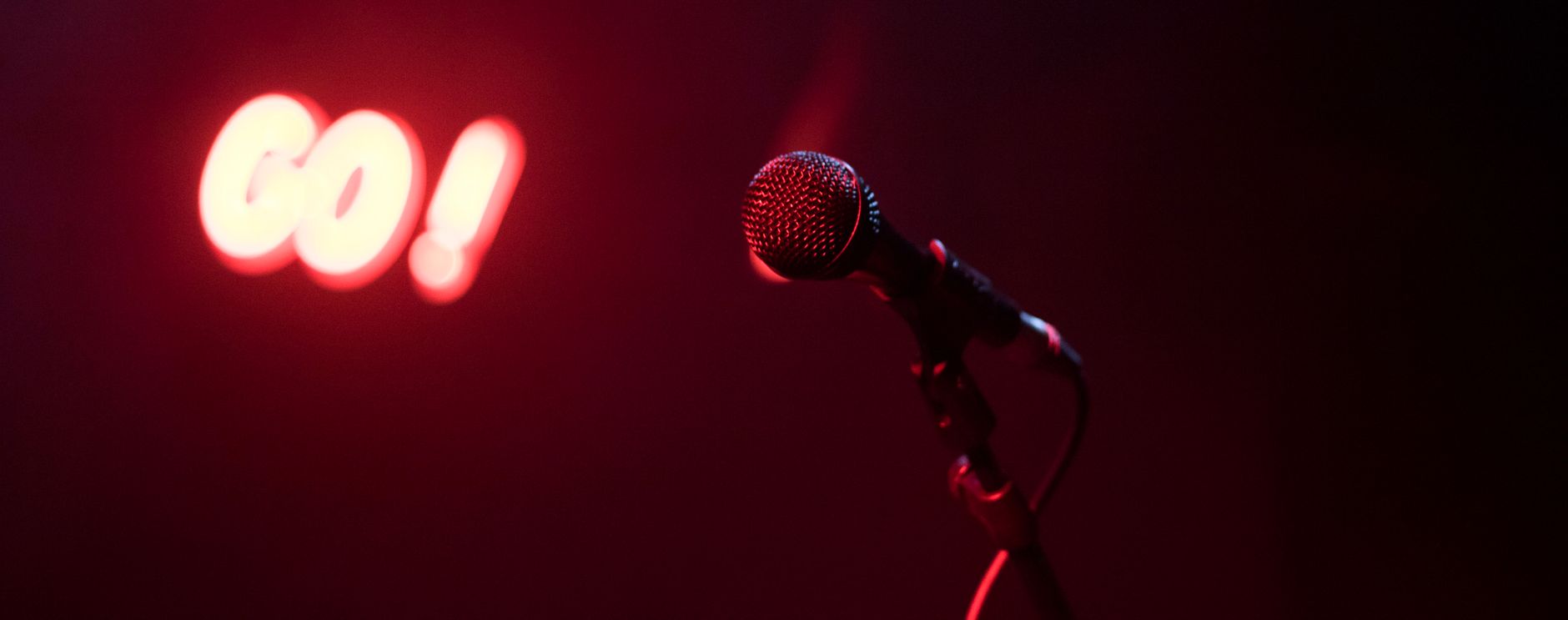 Imagem ilustrativa: Microfone no palco com sinal iluminado em ambiente de show noturno.
