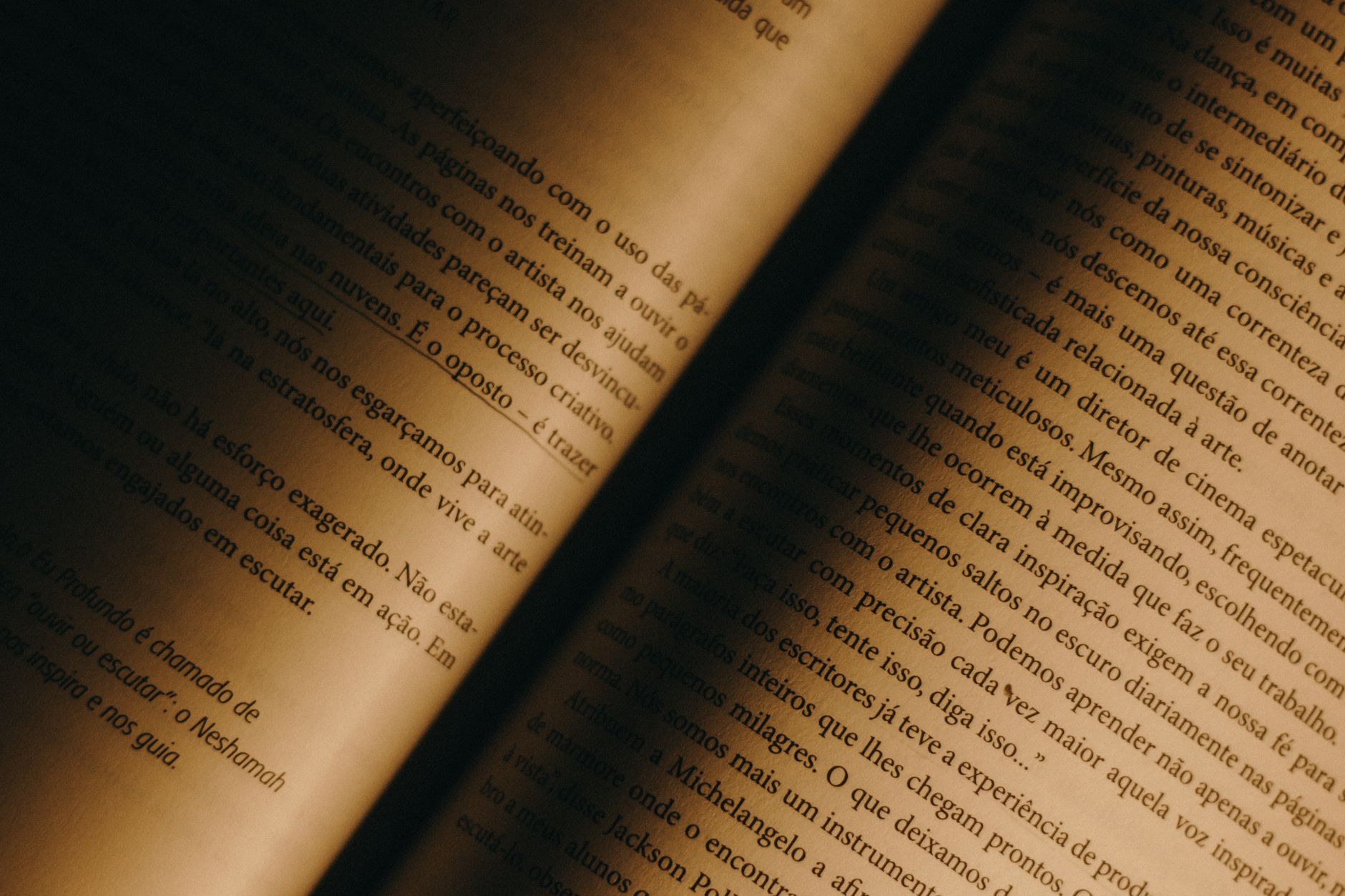 Imagem ilustrativa: Close-up de páginas de livro antigo com iluminação quente, mostrando papel amarelado e texto em português.