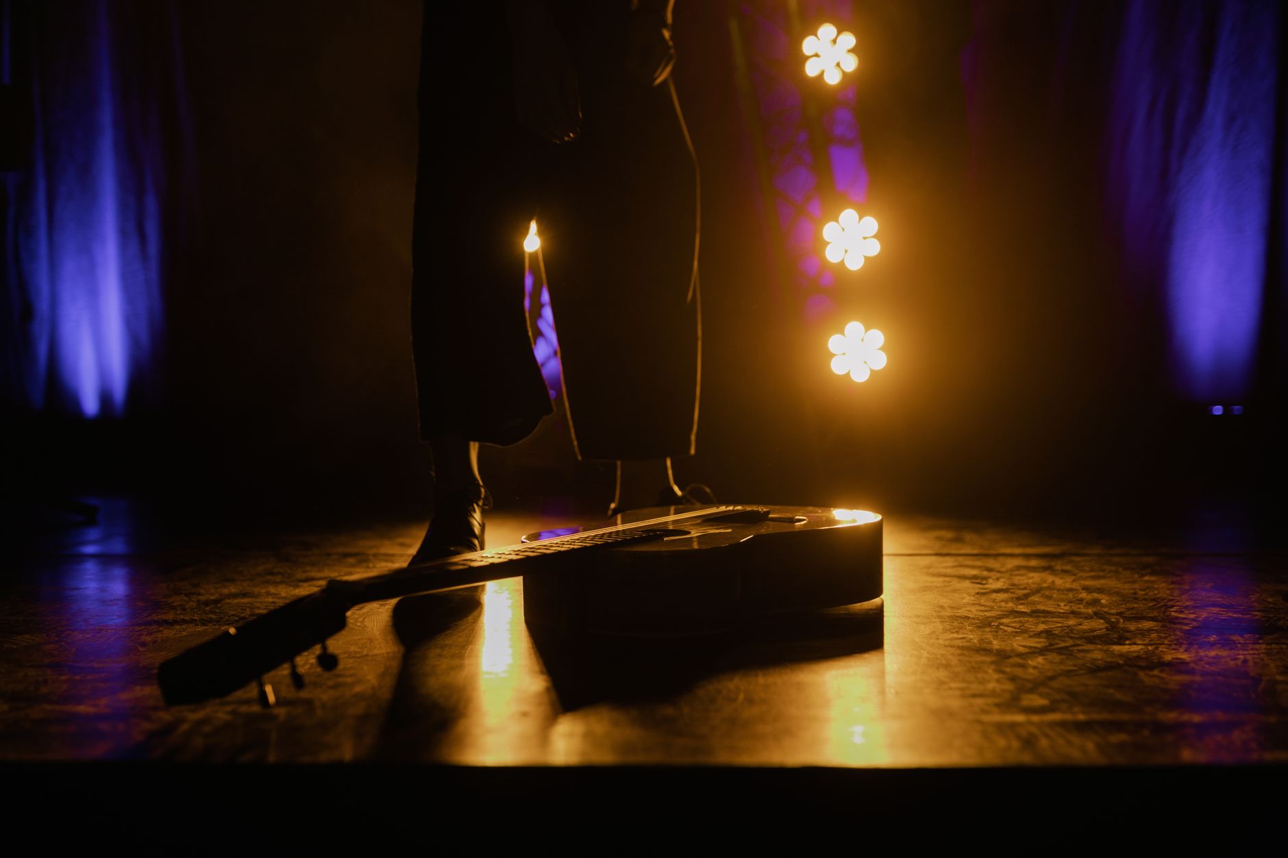 Imagem ilustrativa: Um violão acústico repousa no palco com iluminação dramática criando uma atmosfera envolvente.