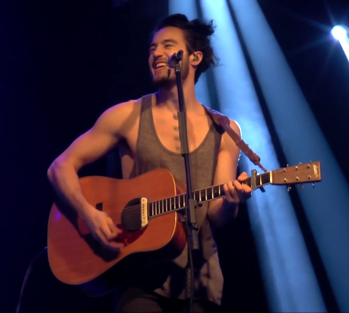 Imagem ilustrativa: Tiago Iorc de regata, cantando e tocando violão em show de 2015