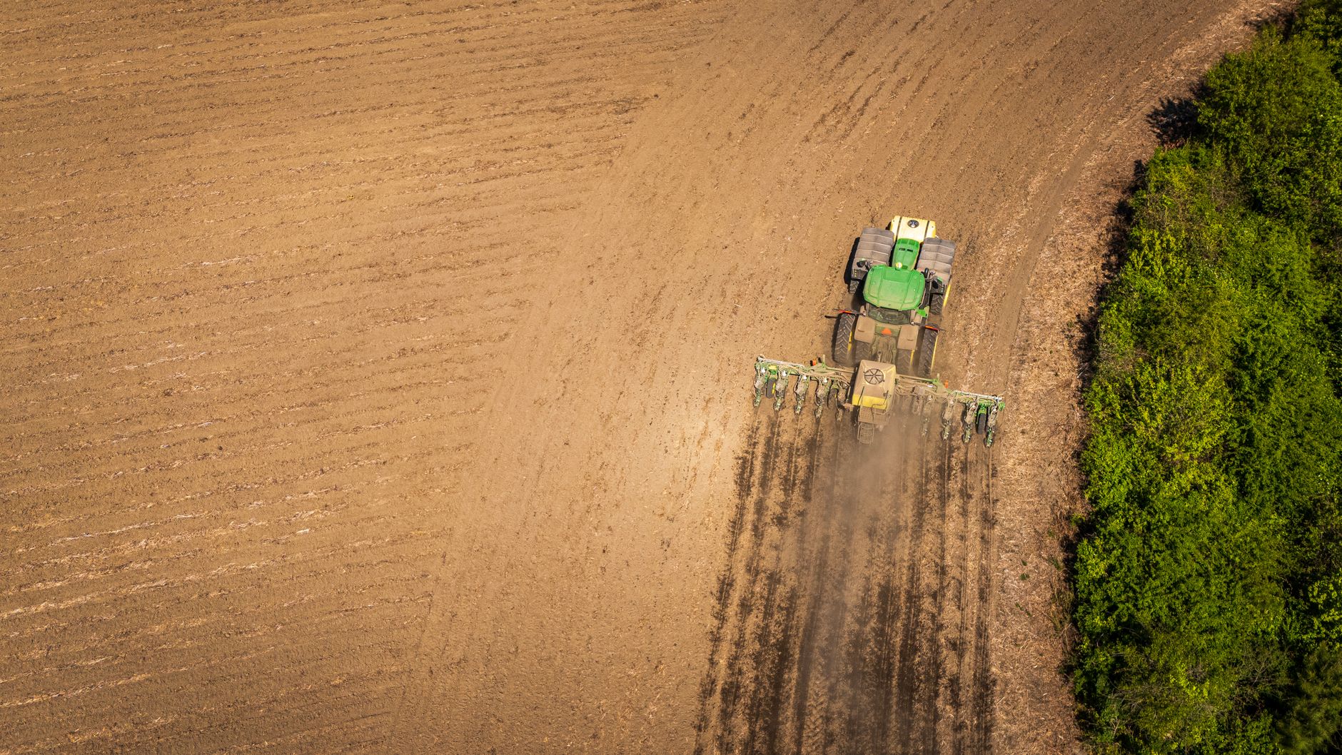 Imagem ilustrativa: Uma imagem aérea de um trator arando terras agrícolas, preparando o solo para o plantio no verão.