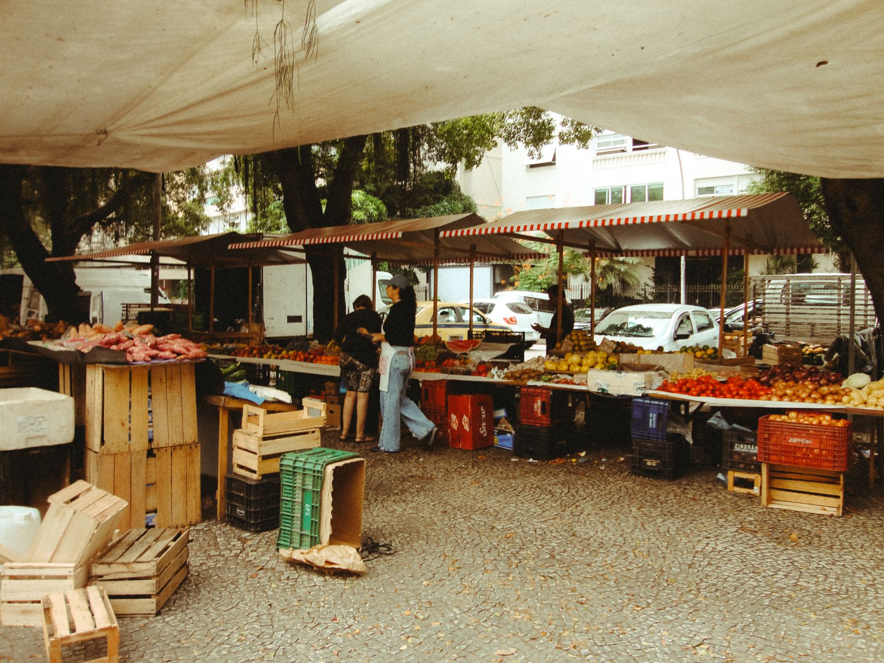 Imagem ilustrativa: Mercado movimentado ao ar livre no Rio de Janeiro com frutas e verduras frescas sob uma cobertura.