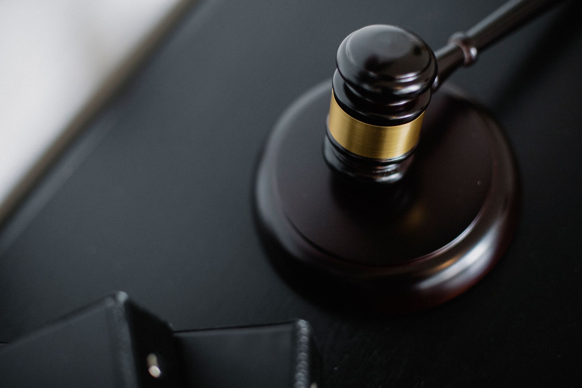 Imagem ilustrativa: Close-up de um martelo de juiz de madeira em uma mesa preta, simbolizando justiça e lei.