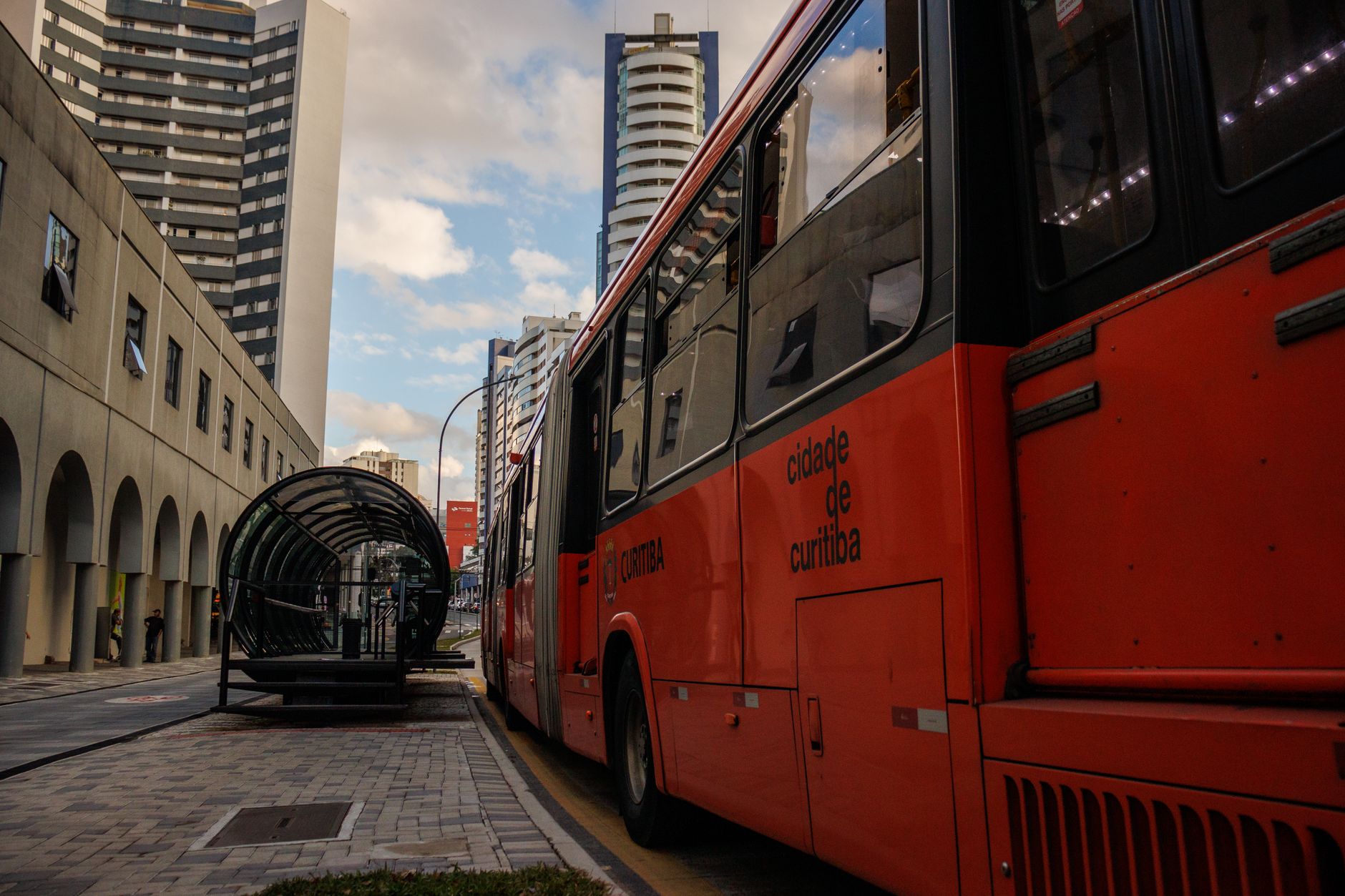 Imagem ilustrativa: Ônibus vermelho do transporte coletivo de Curitiba ao lado de uma estação-tubo, no centro da cidade.