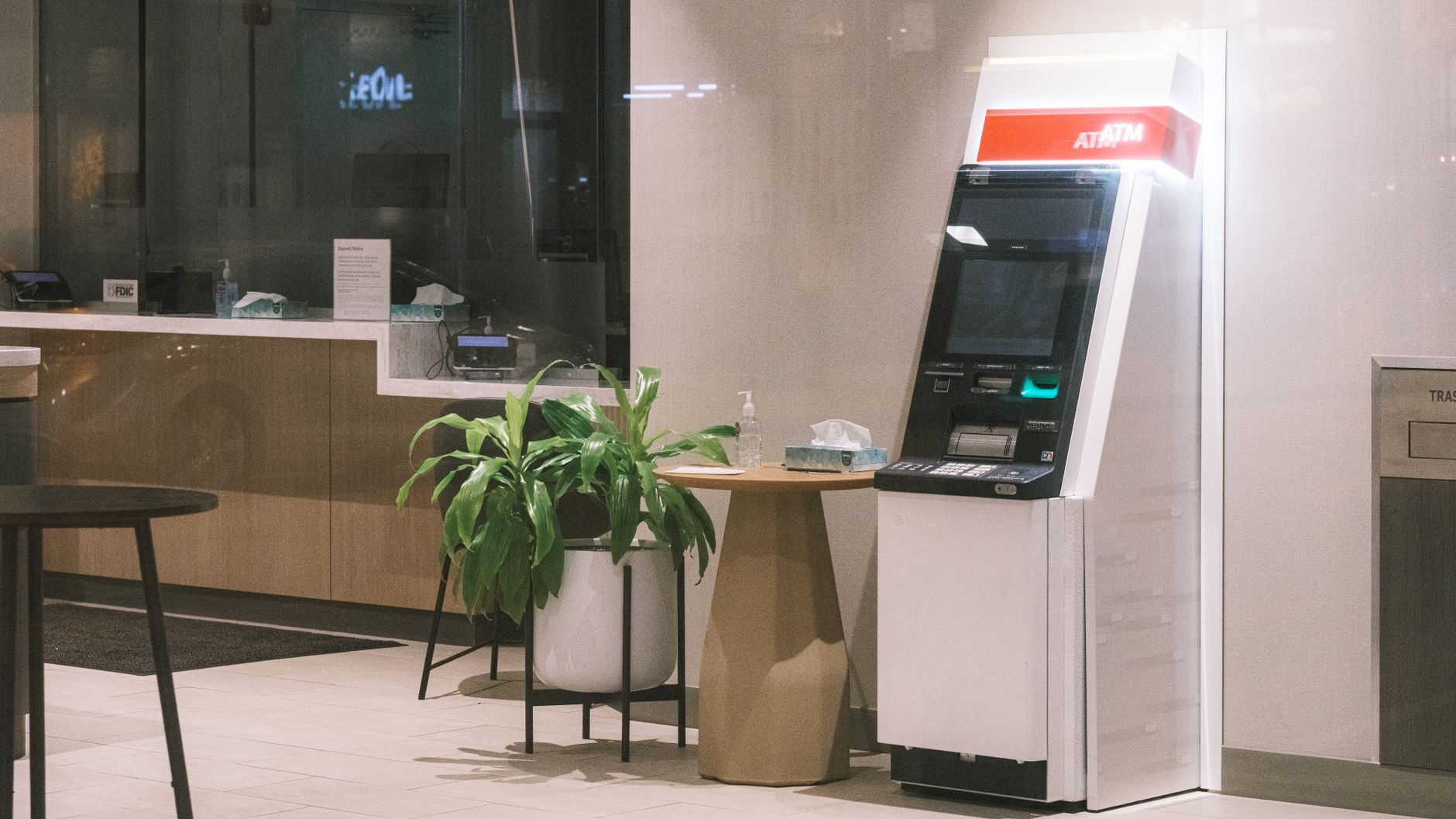Imagem ilustrativa: Uma máquina de ATM está em um lobby moderno de banco, ao lado de uma planta e de uma mesa.