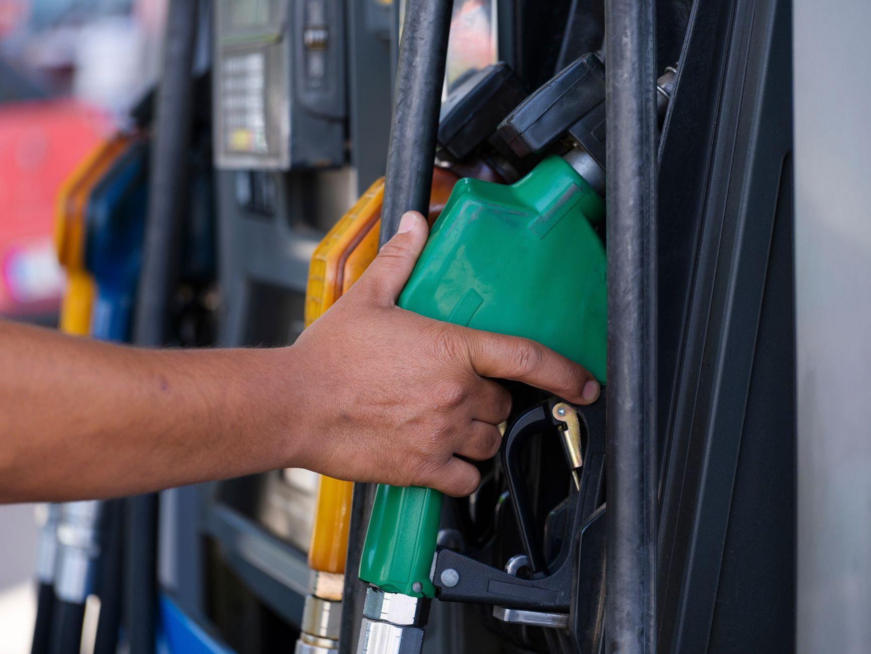 Imagem ilustrativa: Close-up de uma mão segurando um bico de combustível verde em um posto de gasolina.
