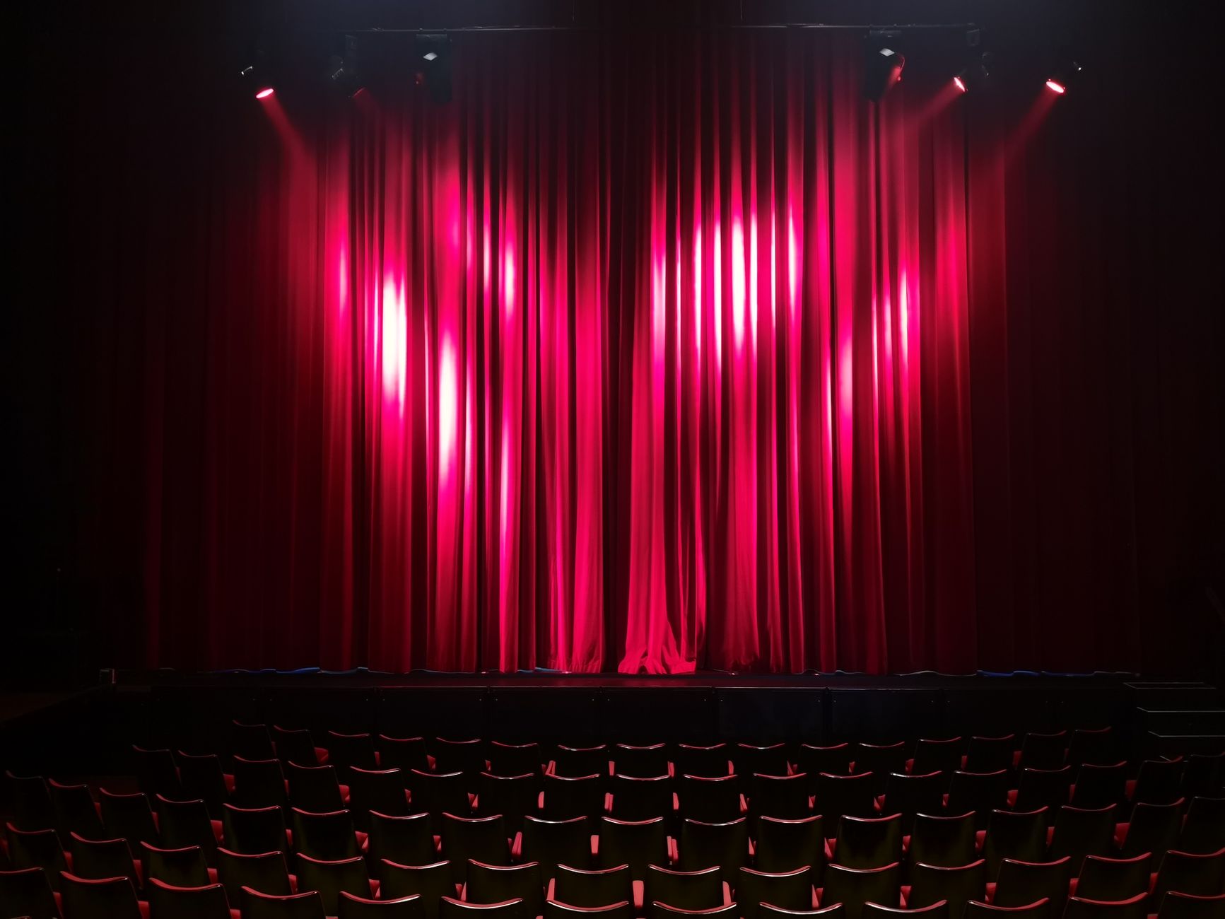 Imagem ilustrativa: Palco de teatro vazio com cortinas vermelhas e assentos, pronto para uma apresentação.