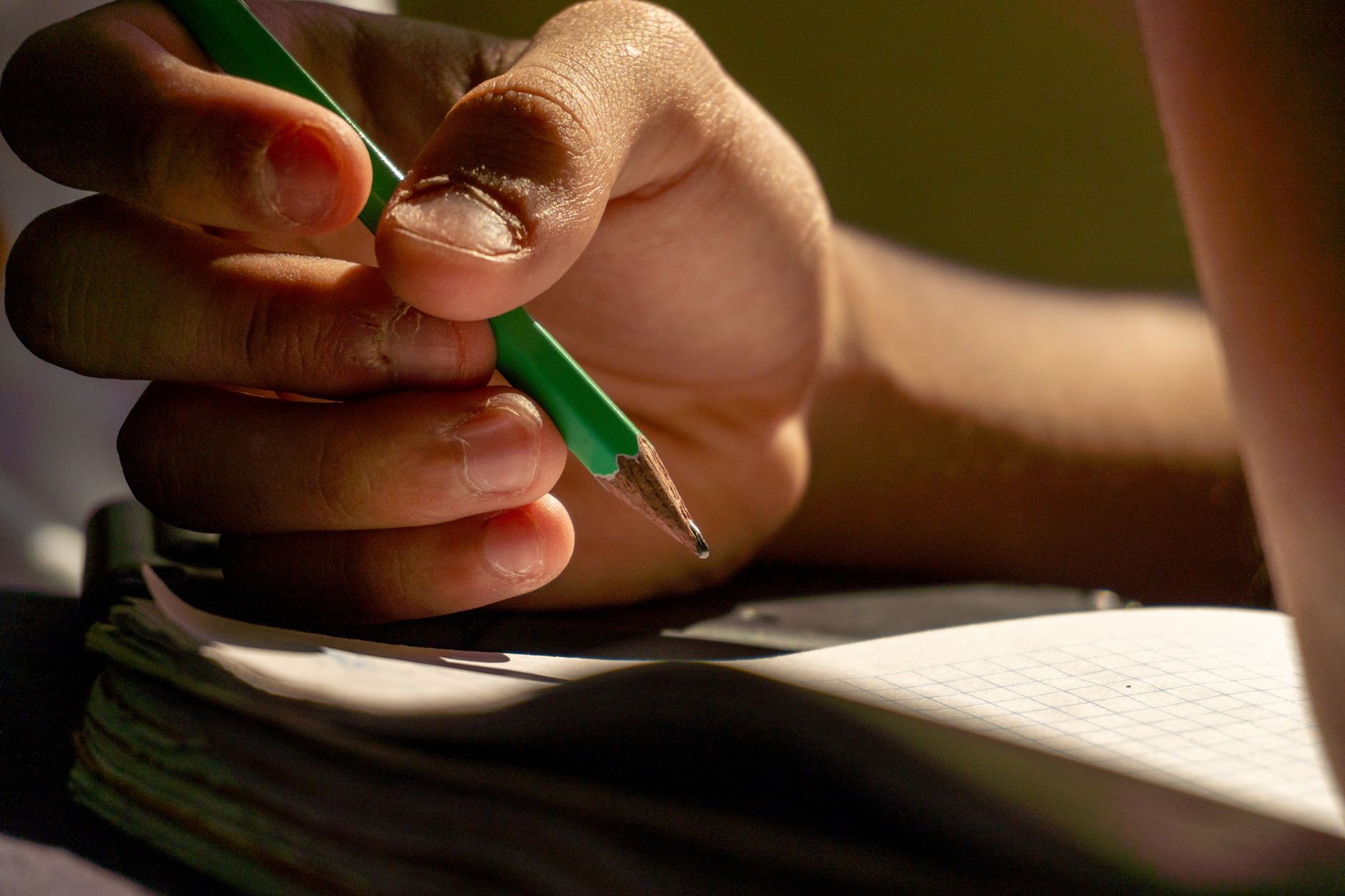 Imagem ilustrativa: Detalhe da escrita à mão com lápis em um caderno, sugerindo estudo ou criatividade.