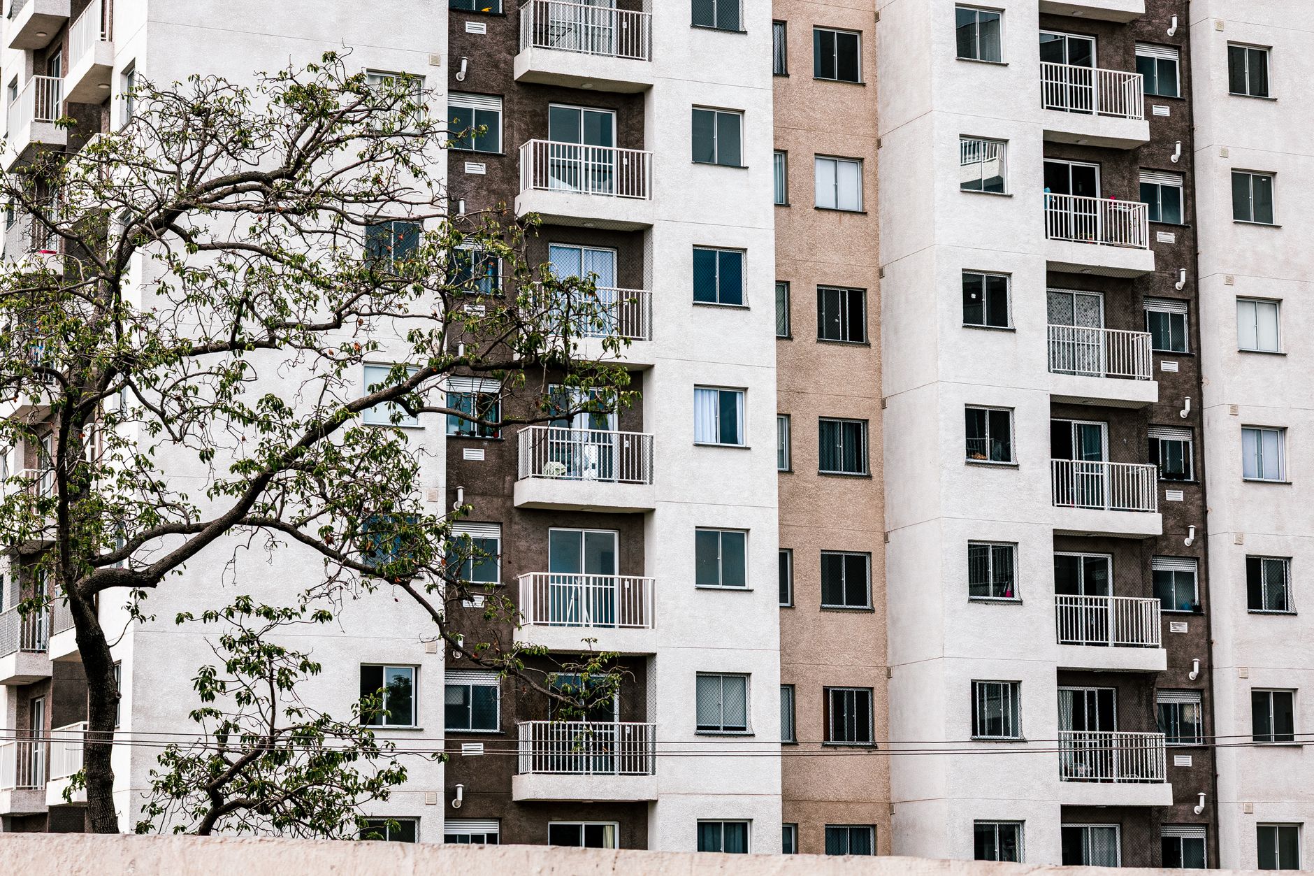 Imagem ilustrativa: Vista exterior de um prédio de apartamentos moderno com varandas e uma árvore, que ilustra a arquitetura urbana.
