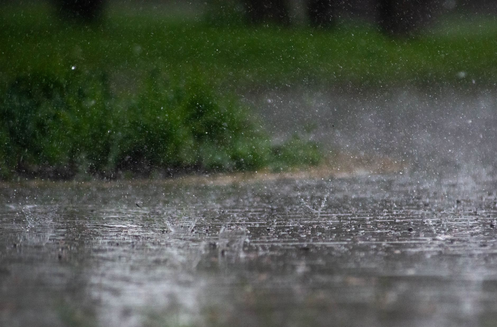 Imagem ilustrativa: Chuva forte respingando no pavimento externo, com vegetação ao fundo.