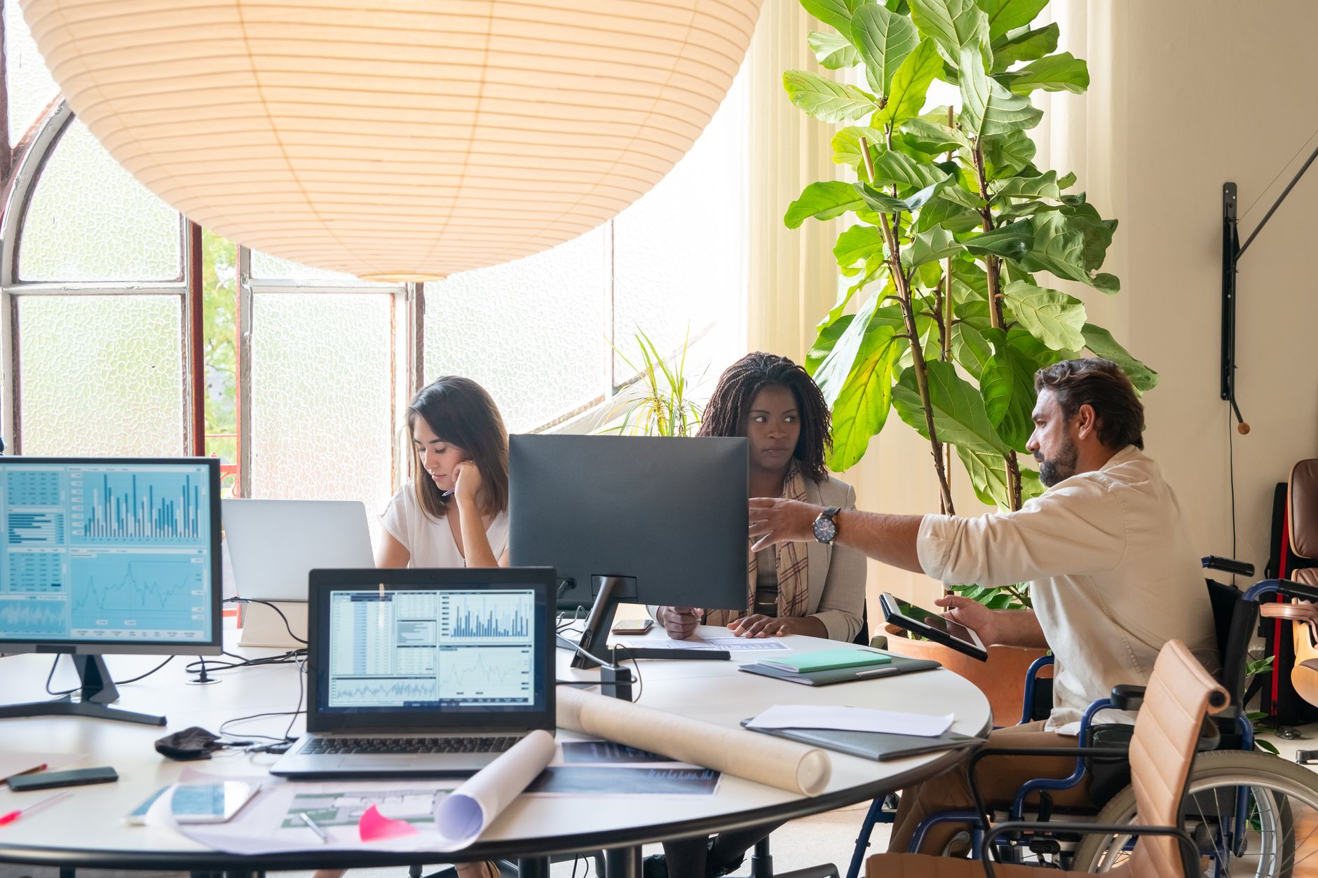 Imagem ilustrativa: Equipe de trabalho em escritório com colega cadeirante à mesa, em ambiente acessível