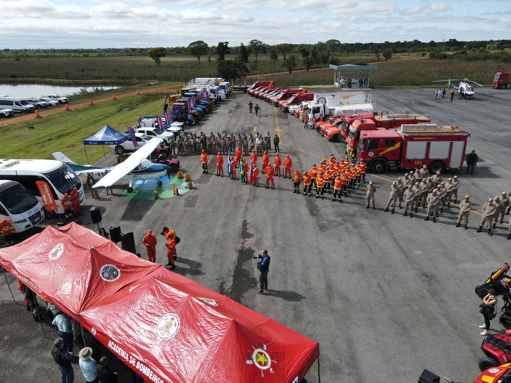 Imagem ilustrativa: Vista aérea de uma equipe de combate a incêndio reunida com caminhões de bombeiros, equipamentos e tendas ao ar livre.