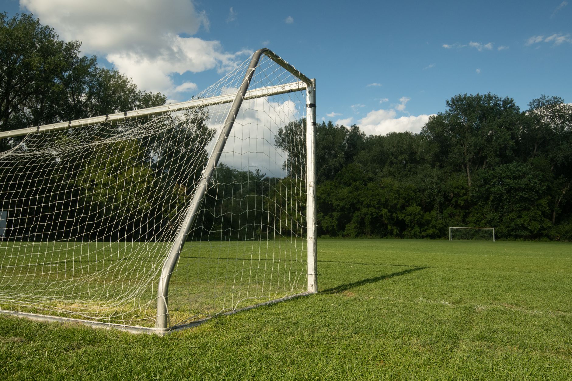 Imagem ilustrativa: Trave e rede de futebol em campo de grama com iluminação natural.