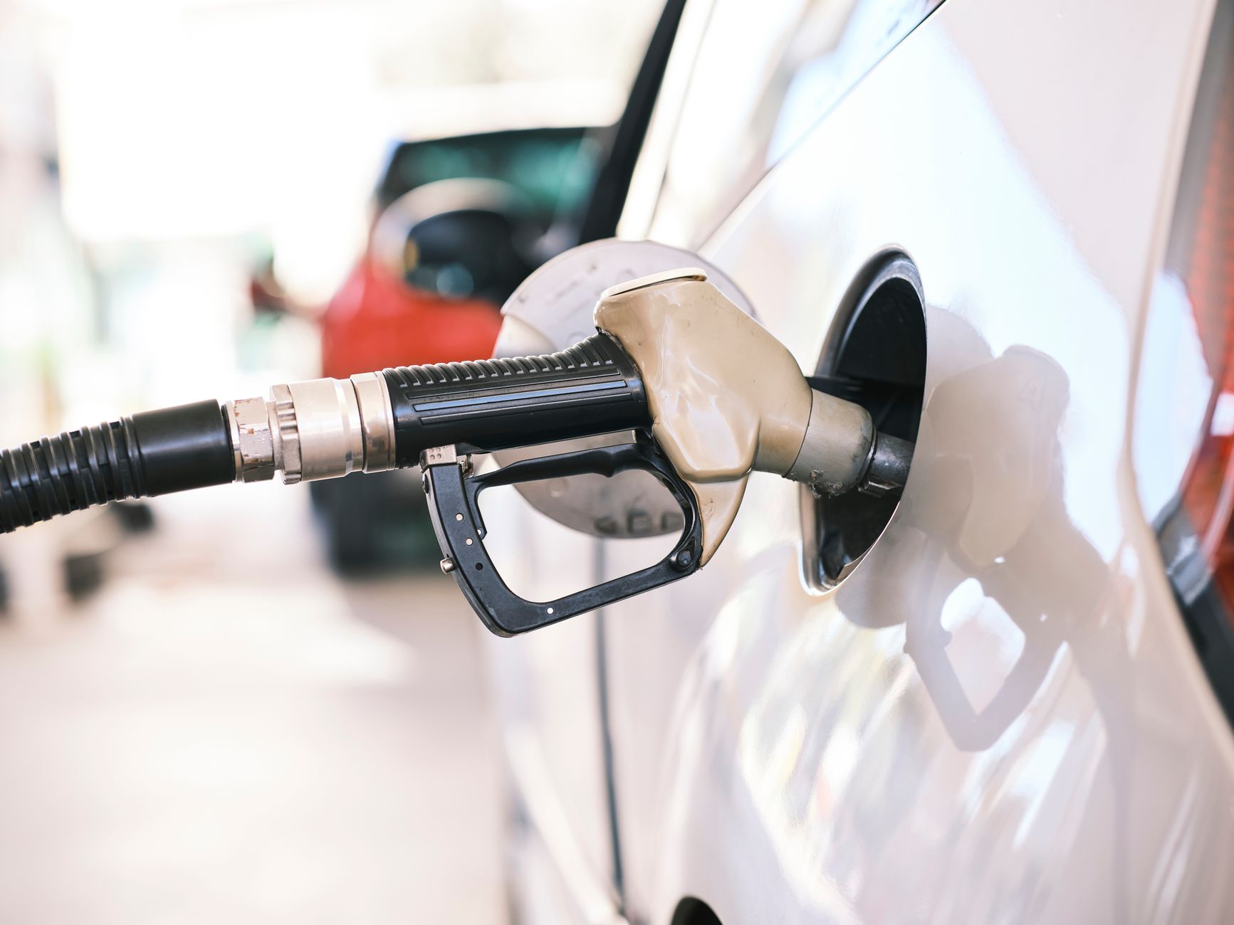 Imagem ilustrativa: Bico de abastecimento inserido em carro em um posto de gasolina, vista de perto enfatizando temas de energia e transporte.