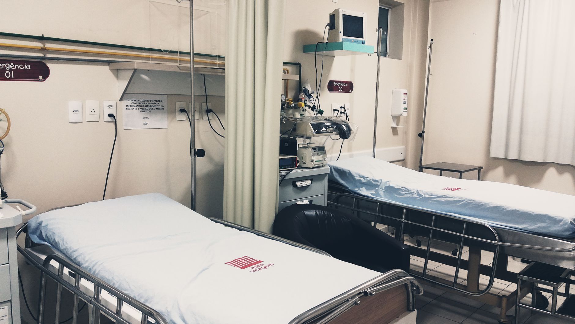 Imagem ilustrativa: Um quarto de hospital vazio equipado com duas camas, equipamentos de monitoramento e iluminação ambiente.