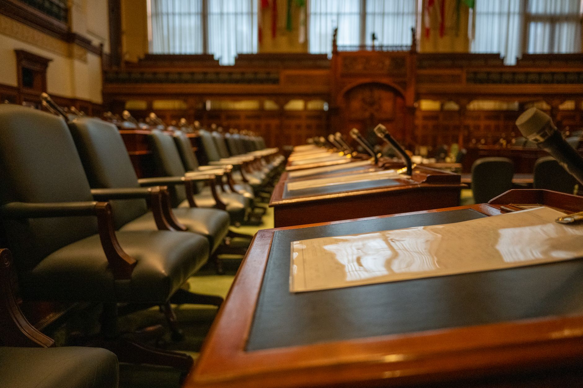 Imagem ilustrativa: Uma vista detalhada de uma câmara legislativa vazia com fileiras de mesas e microfones.
