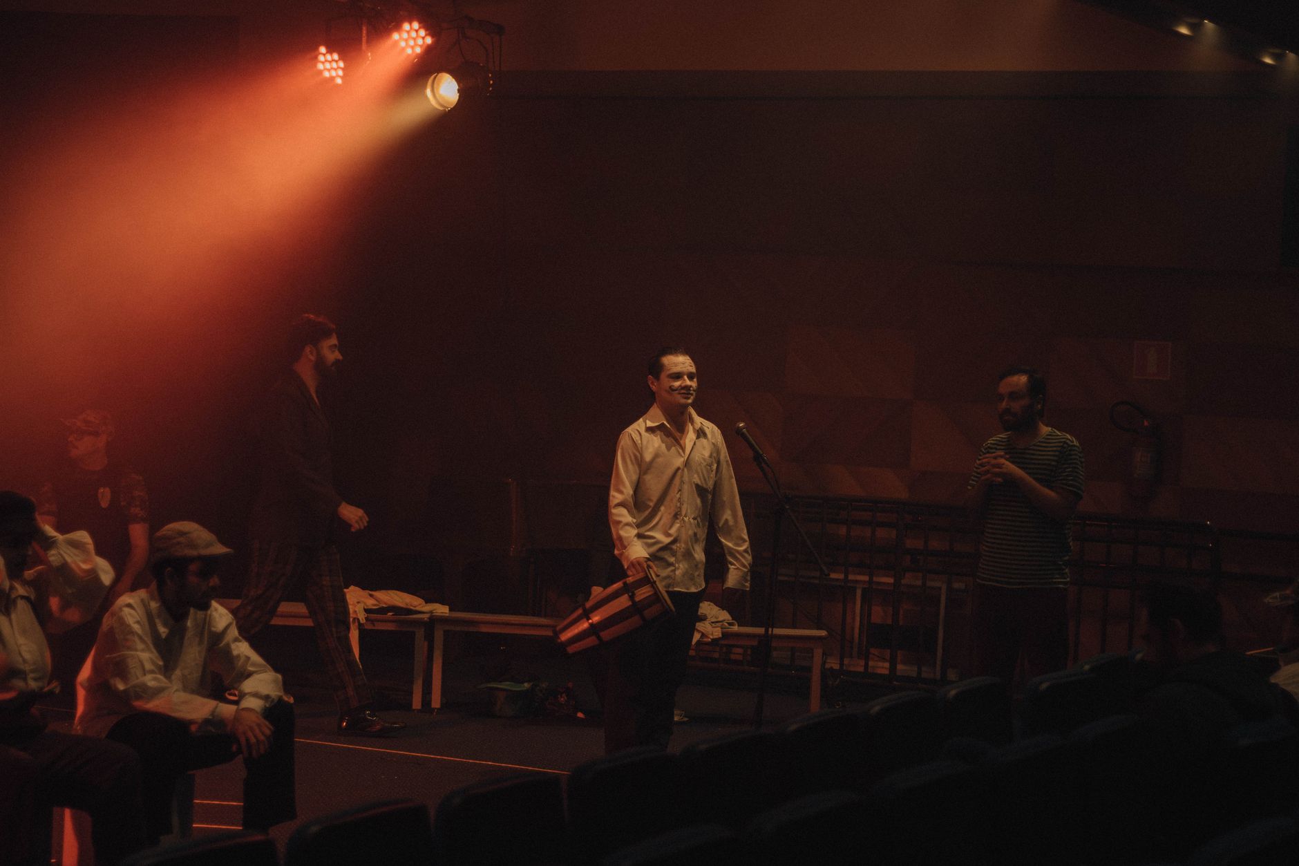 Imagem ilustrativa: Atores em cena num palco de teatro com pouca luz, sob refletores de luz quente