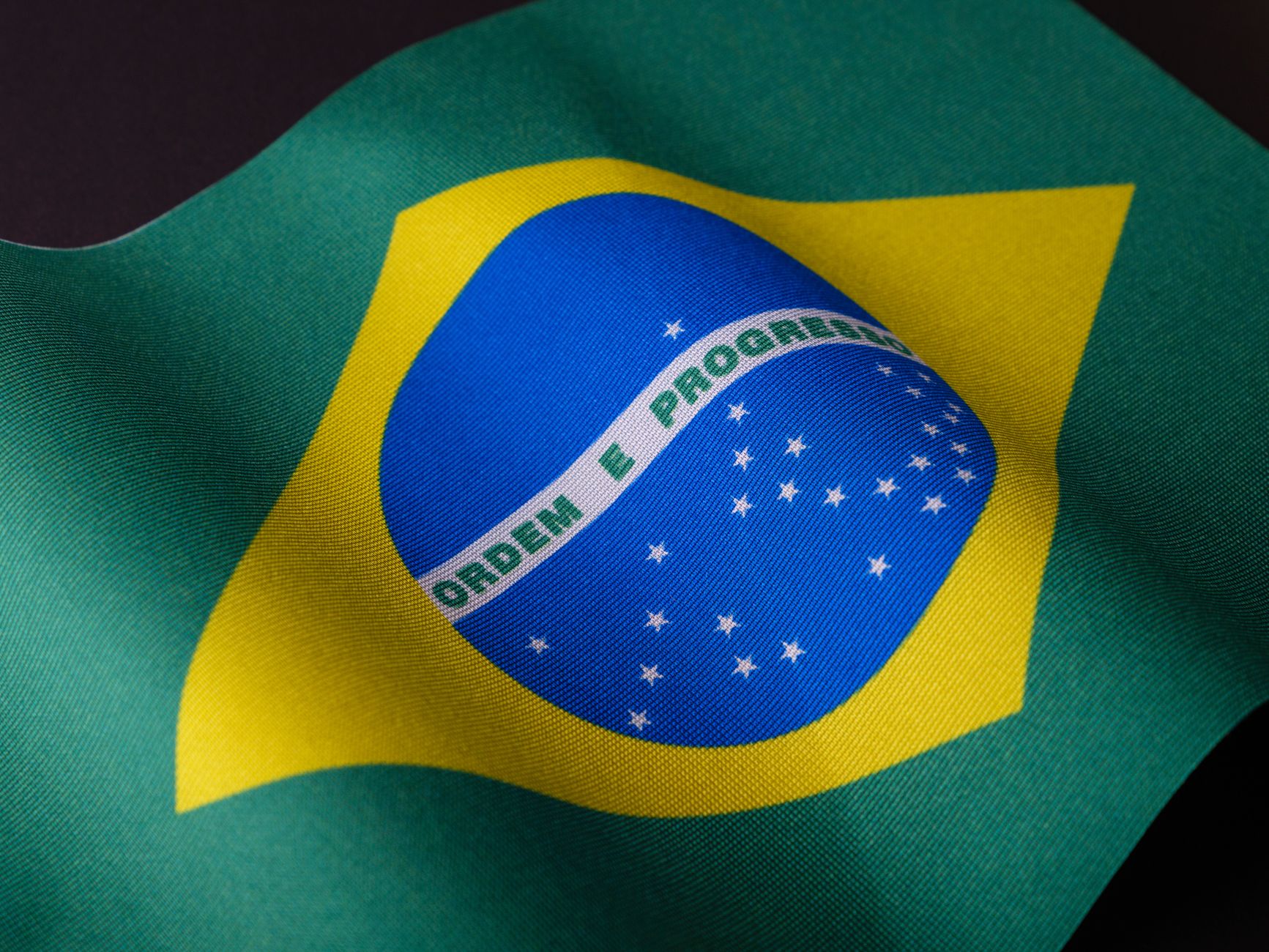 Imagem ilustrativa: Imagem detalhada da bandeira brasileira destacando cores vibrantes e emblema.