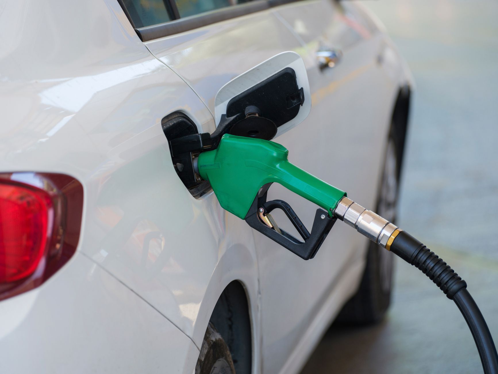 Imagem ilustrativa: Close-up de um bico verde abastecendo um carro branco em um posto de gasolina.