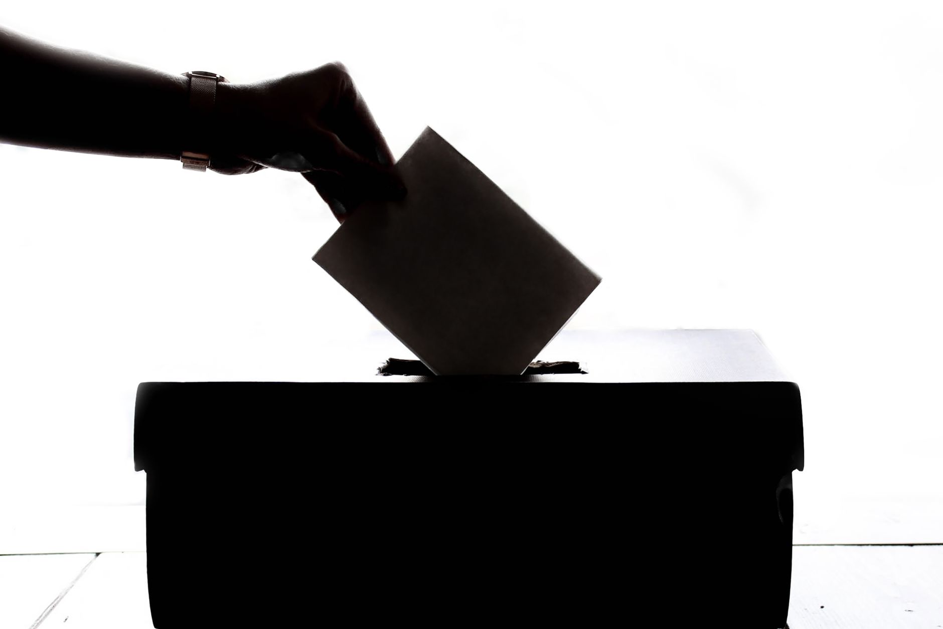 Imagem ilustrativa: Silhueta de uma mão colocando um voto em uma urna, simbolizando a democracia.