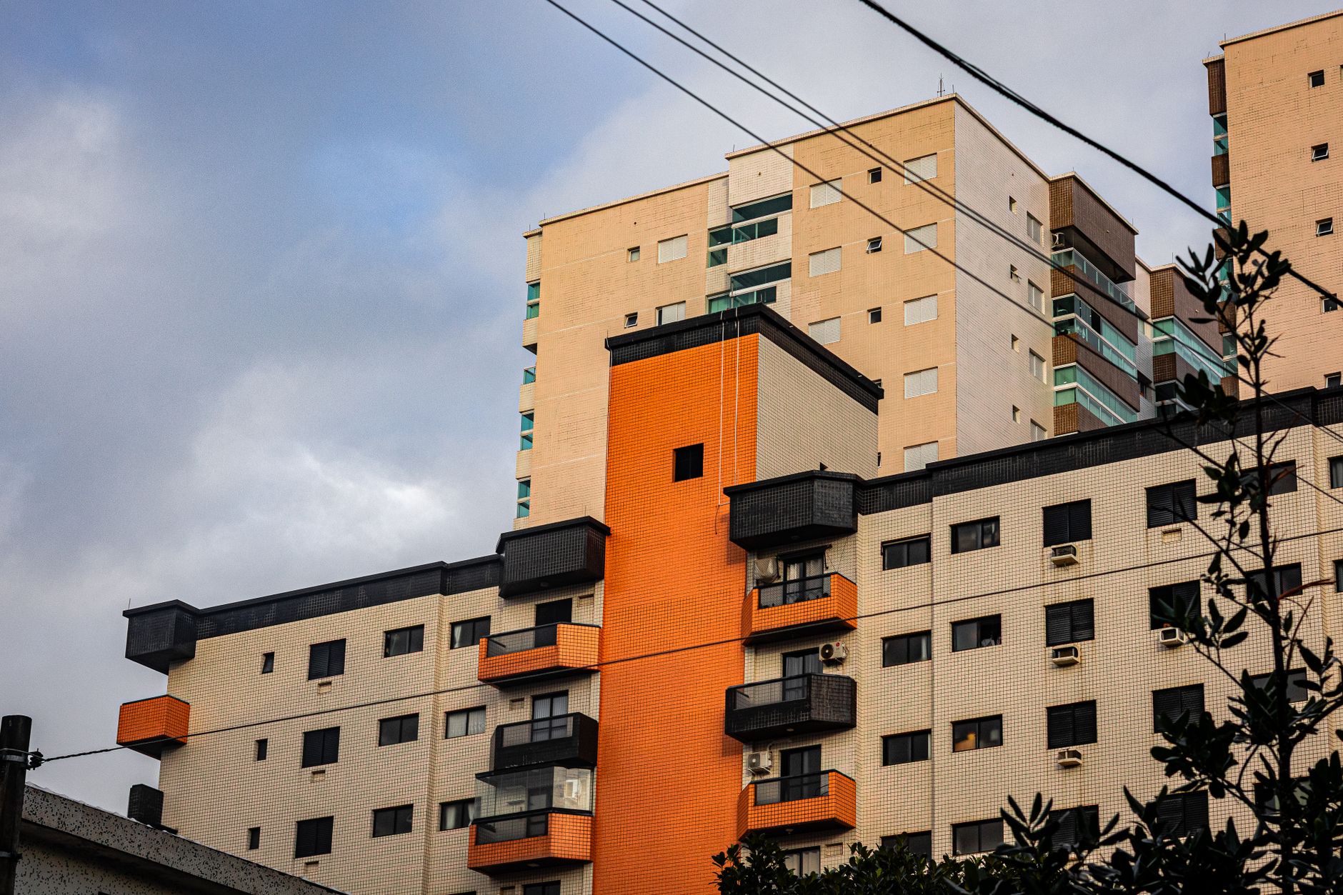 Imagem ilustrativa: Prédio residencial de vários andares com varandas e fachada laranja, sob céu nublado