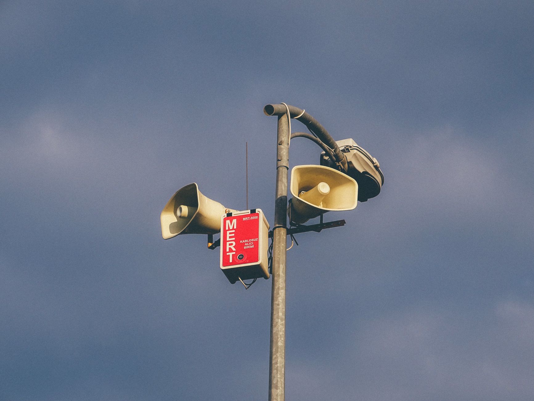 Imagem ilustrativa: Um sistema de alerta com alto-falantes em um poste contra um céu nublado, sinalizando avisos de emergência.