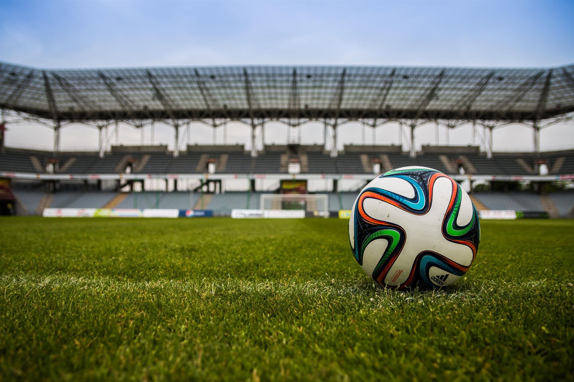 Imagem ilustrativa: Close-up de uma bola de futebol em um campo de grama exuberante com um estádio vazio ao fundo.