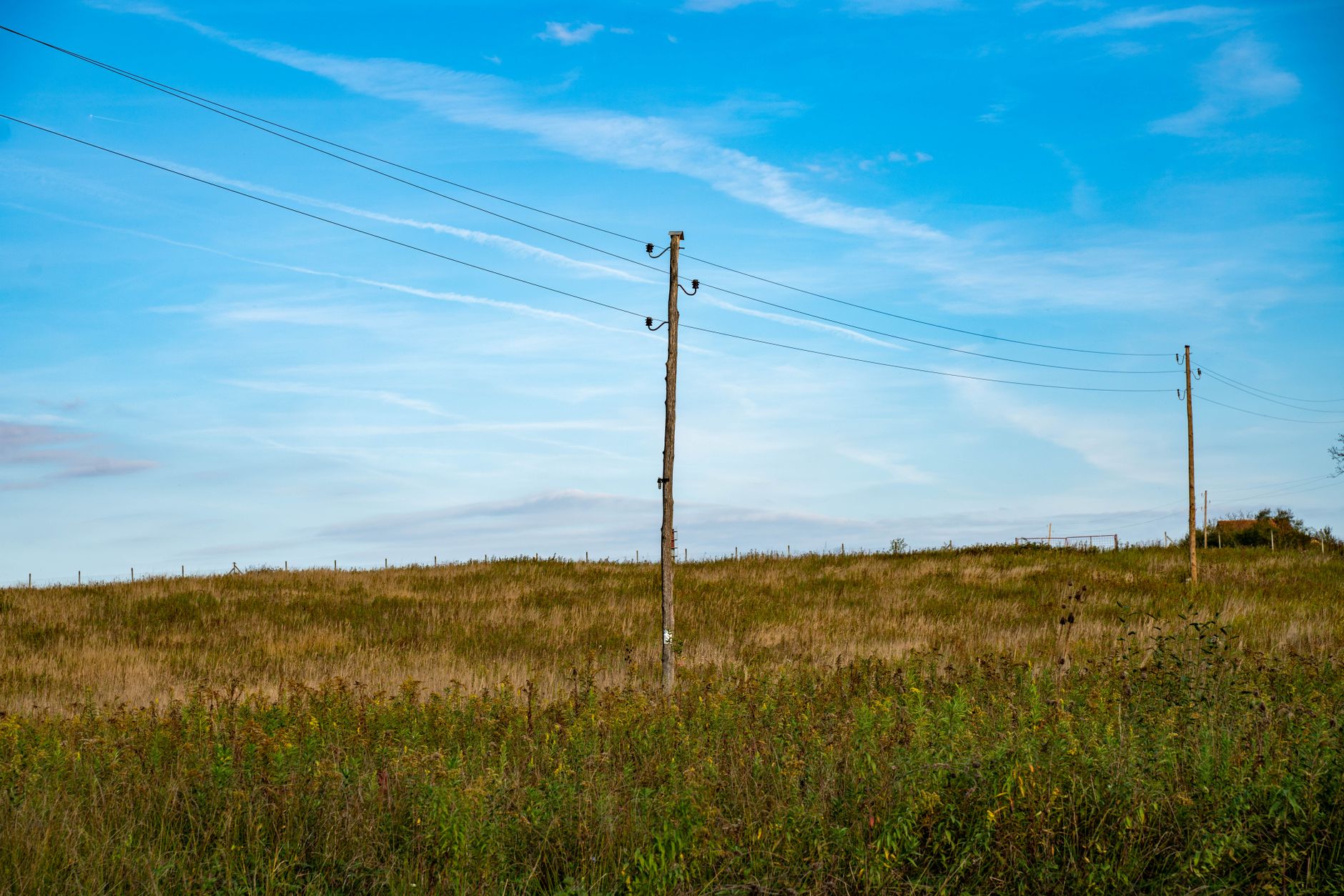 Imagem ilustrativa: Cena pacífica do campo com postes elétricos em meio a um vasto campo verde sob um céu azul.