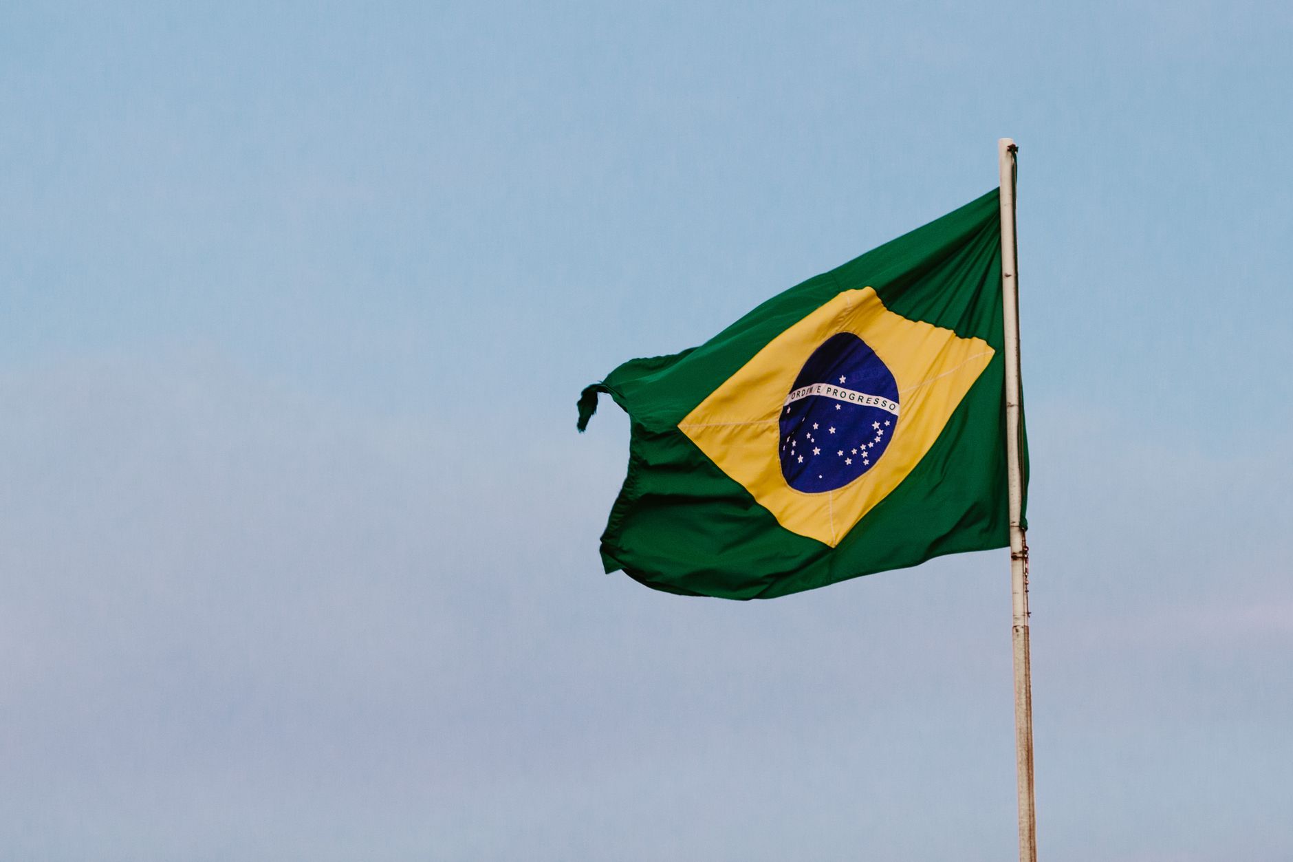 Imagem ilustrativa: Uma bandeira brasileira balançando graciosamente contra um céu azul claro, simbolizando orgulho nacional e patriotismo.