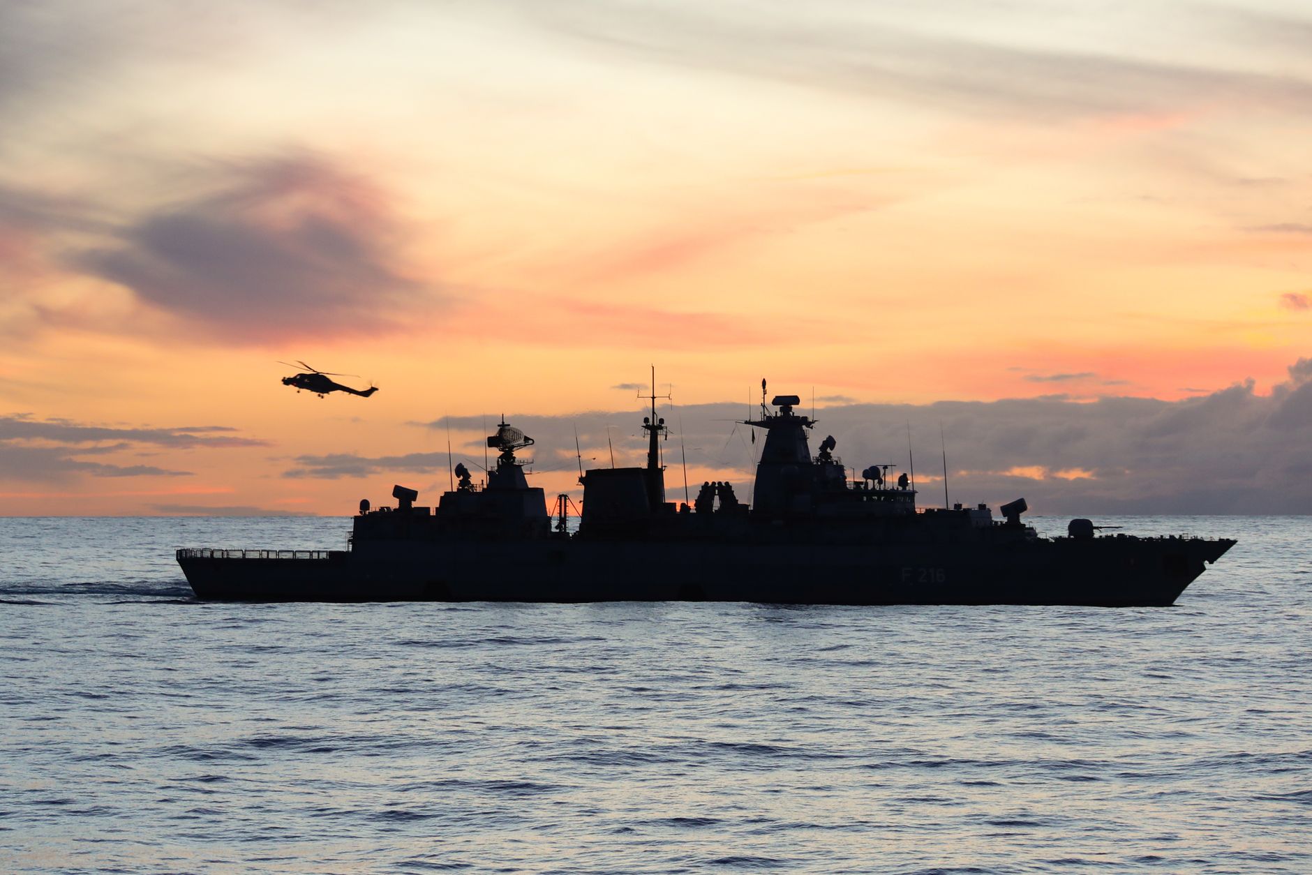 Imagem ilustrativa: Silhueta de um navio de guerra e helicóptero no mar durante o pôr do sol.